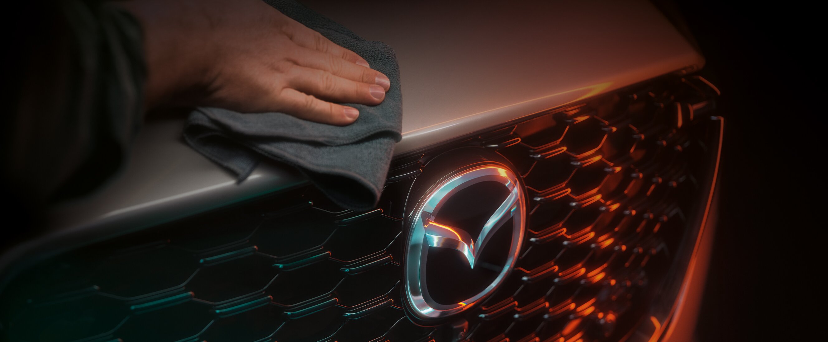 Mazda Crossover Modell in gedämmtem Licht, bei dem eine Hand mit einem grauen Tuch über die Front wischt.